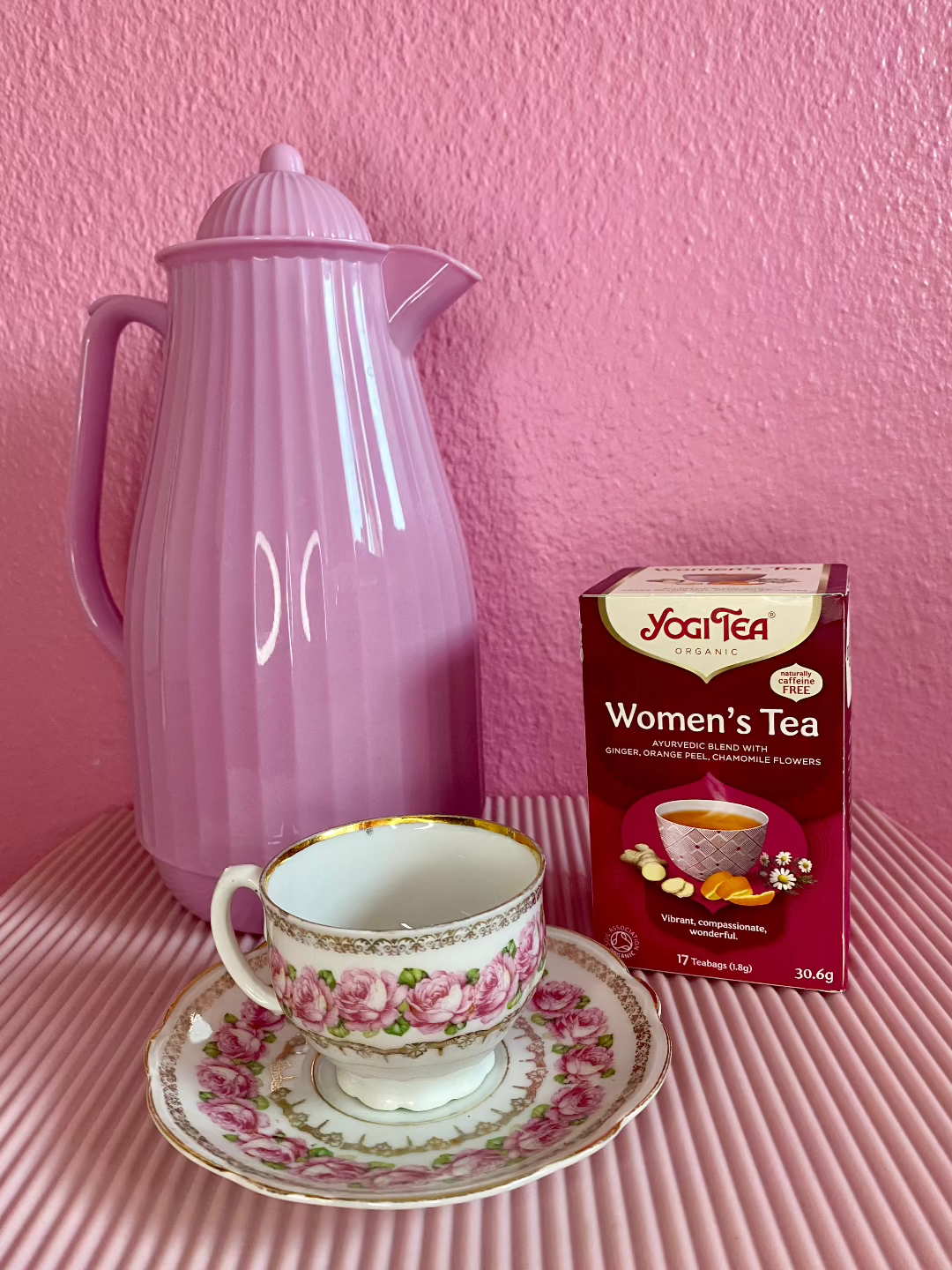 En bakke med en lyserød the kande, en pakke women's tea og en fin tekop med guldkant og lyserøde roser på.